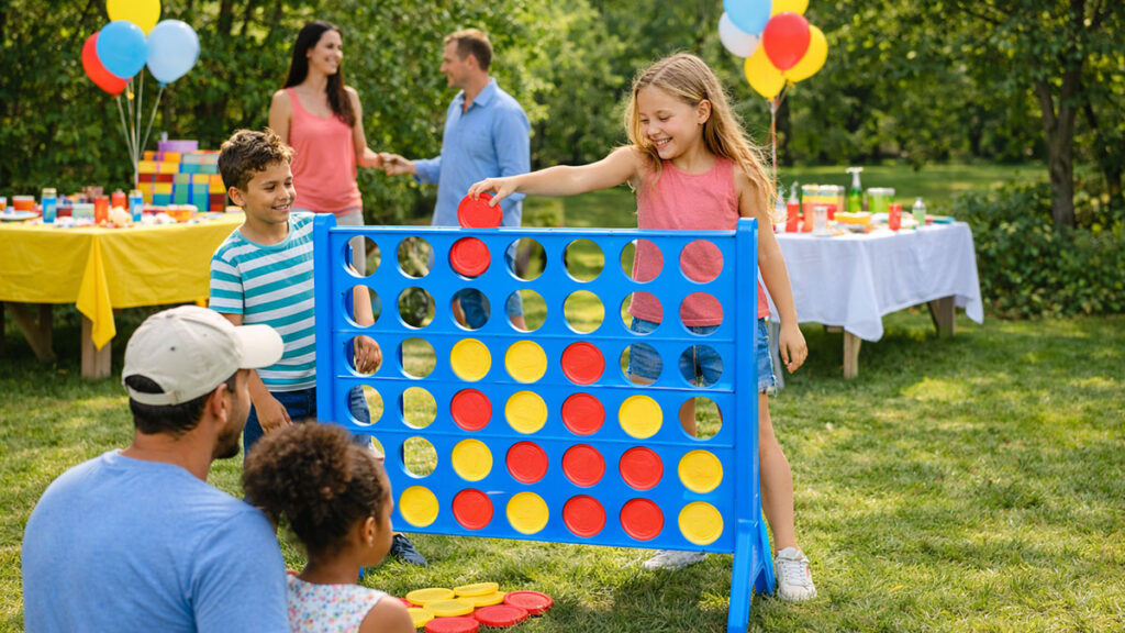 Kids playing a jumbo connect four game at a backyard party