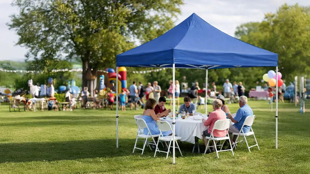 A group of people sitting at a table underneath a pop-up tent at an outdoor party